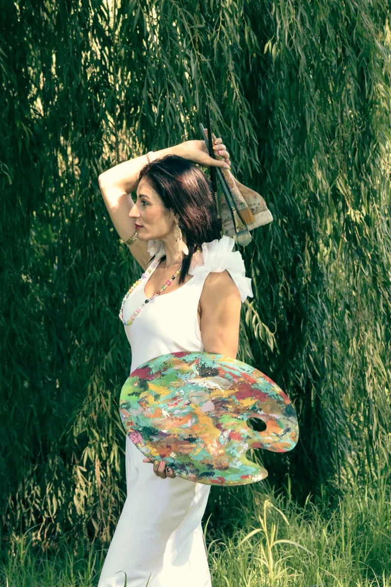 Jullie-Ann Viljoen holding her palette and paintbrushes beneath a willow tree