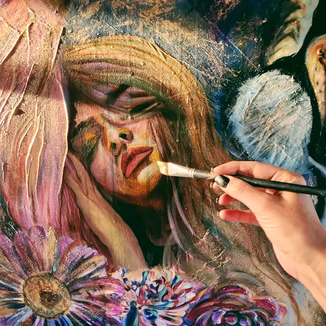 Jullie-Ann's hand painting a woman's face on canvas with a fine brush